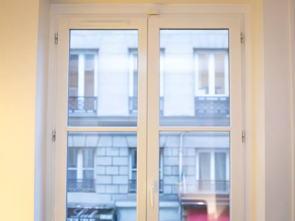 Fenêtre à deux battants peinte en blanc ouvrant sur une façade haussmannienne