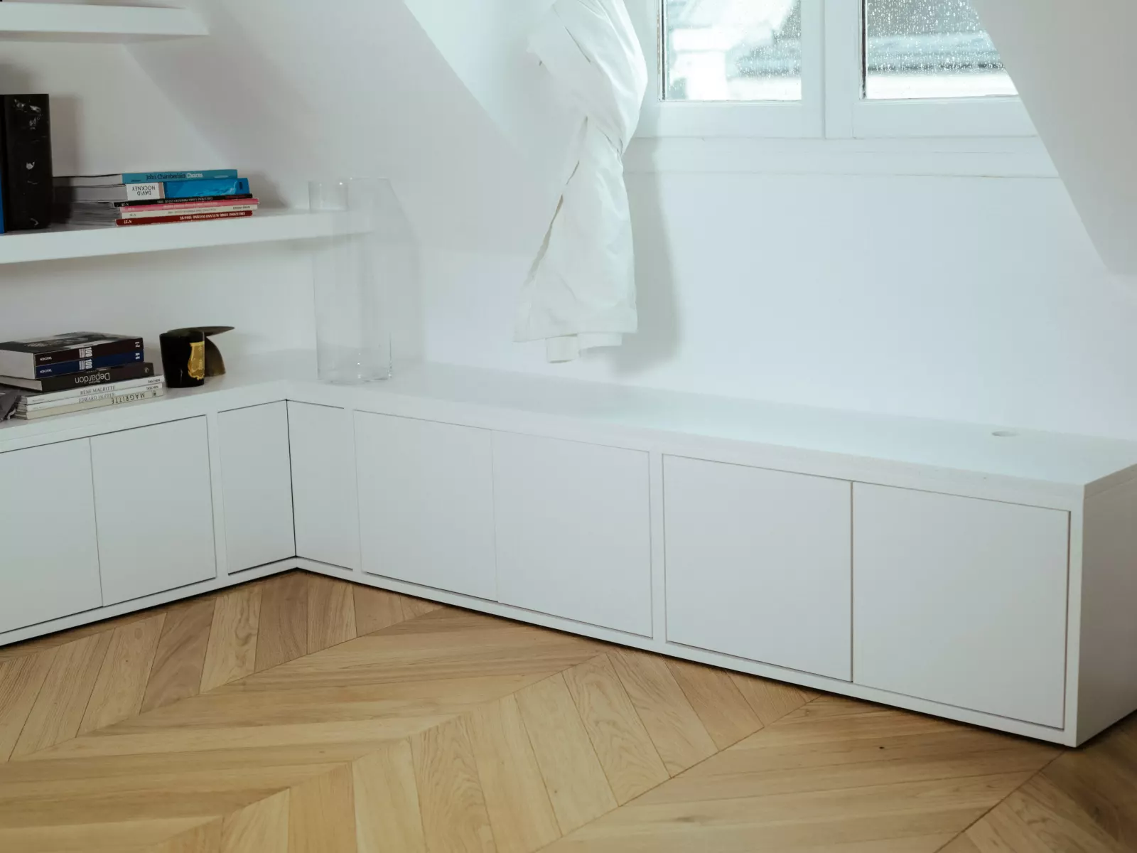 Pièce sous combles aux murs et rangements peints en blanc, parquet point de Hongrie